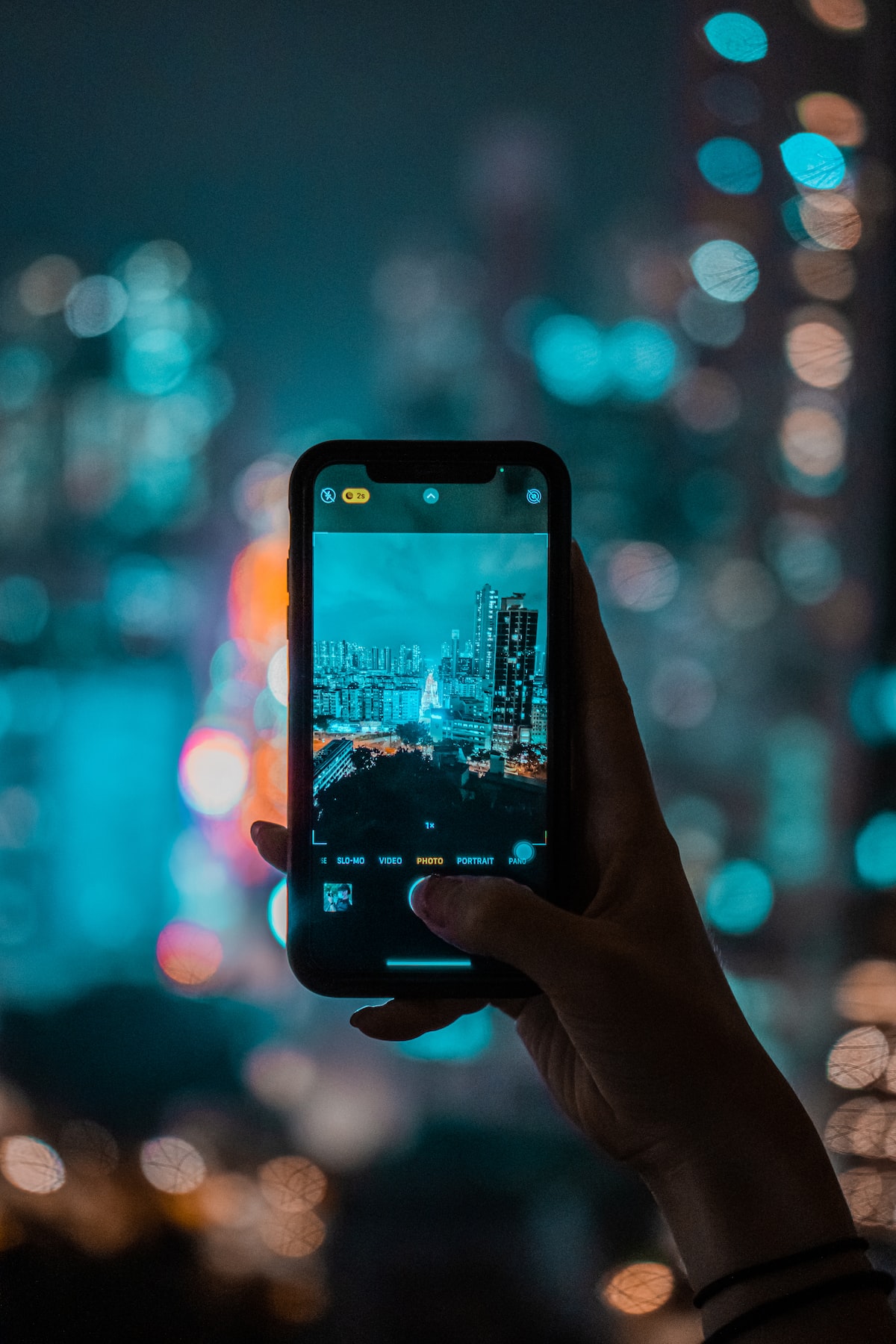 Person holding a smartphone photographing a city skyline at night